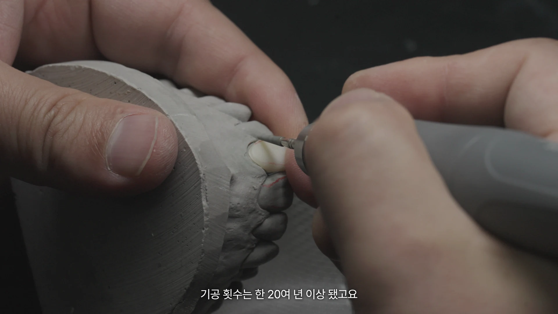 제작물을 손에 쥐고 회전 도구로 다듬는 기공실장의 손